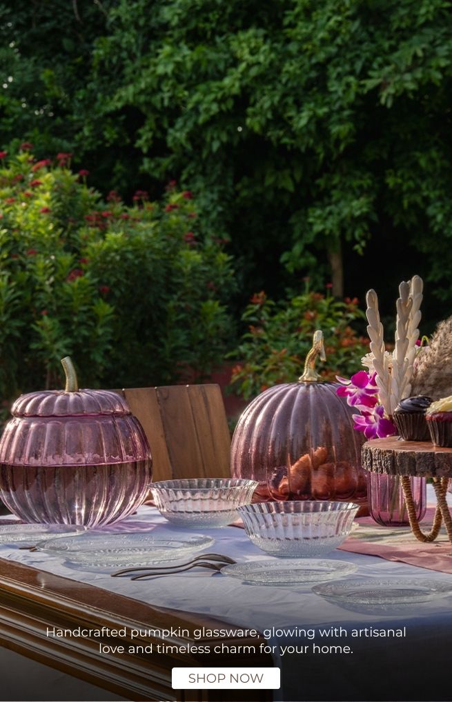 Decorative table setting with pink glass pumpkins and other autumn-themed items outdoors.